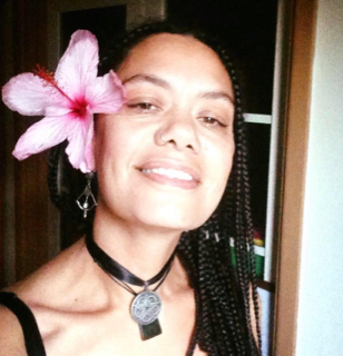 A photo of Alison Bramich, she is facing the camera and has a large pink hibiscus flower behind her ear.